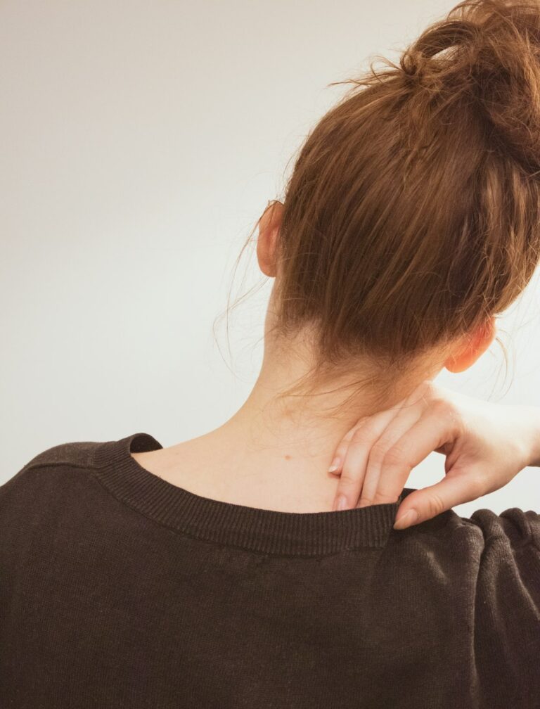 Person seated at a desk gently stretching the neck and shoulders in a bright home setting.